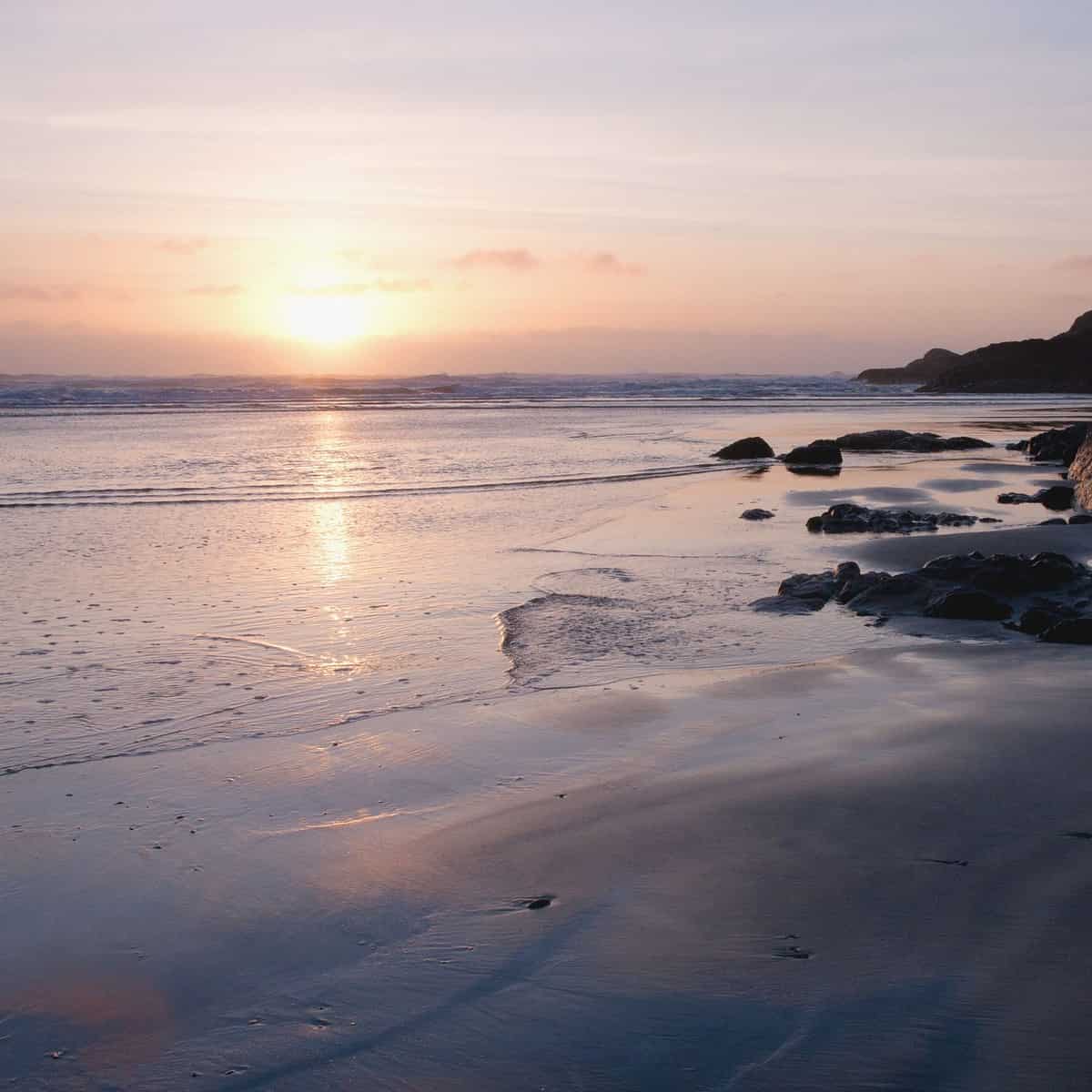 The sunsets over rocks and sand at the beach at Cox Bay Tofino BC