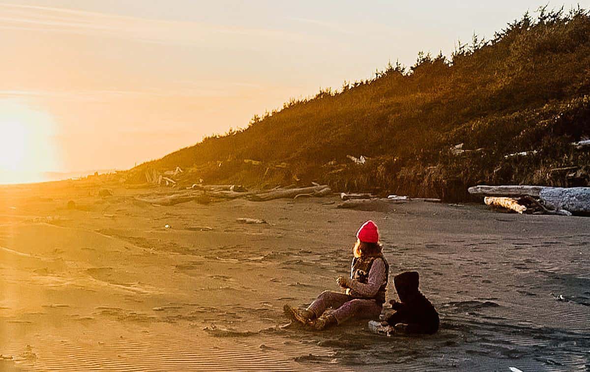 A mom and young child sitting on the sand at a beach in Tofino, Comber's Beach.